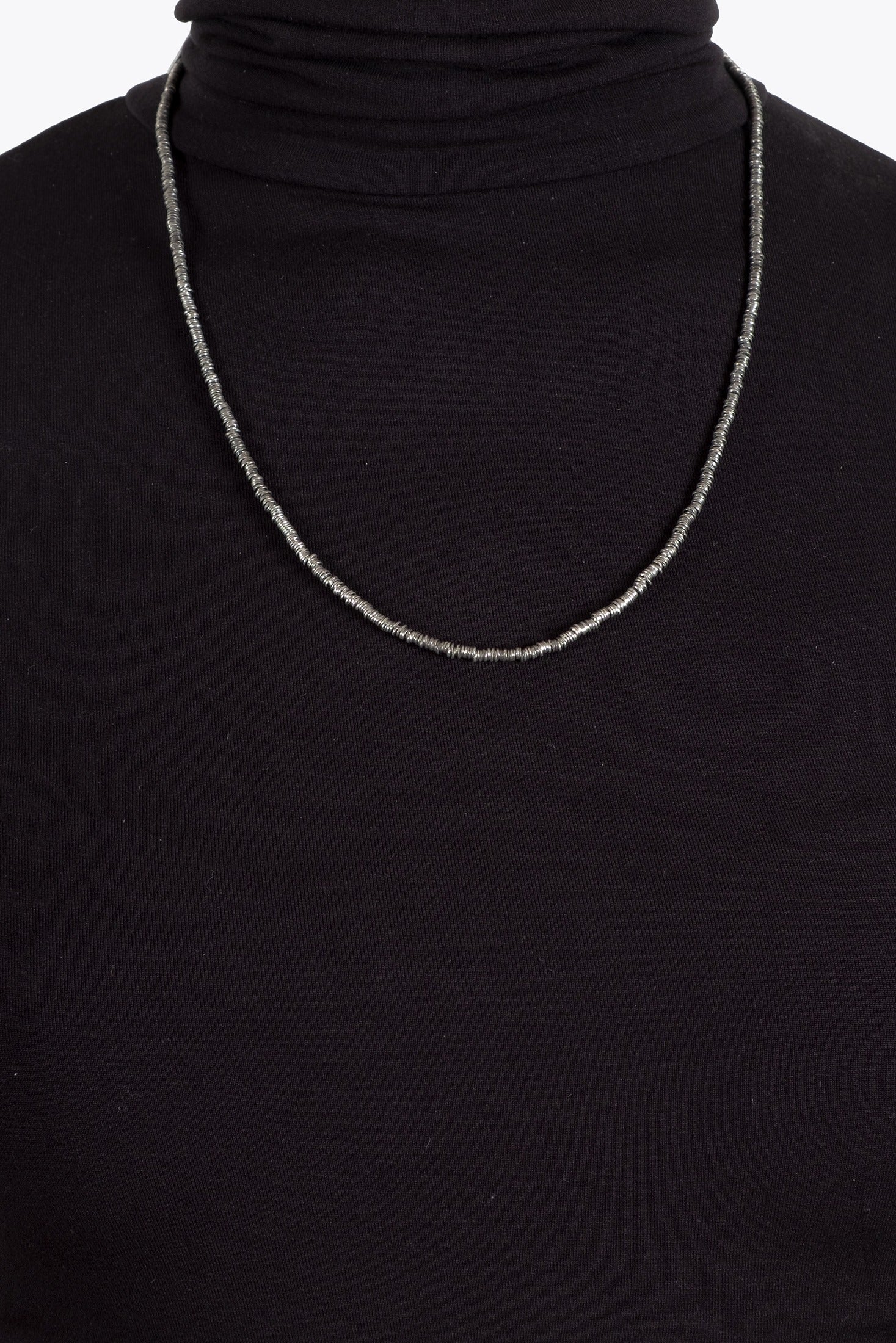 Close-up of a black turtleneck sweater with a silver sequins chain necklace.